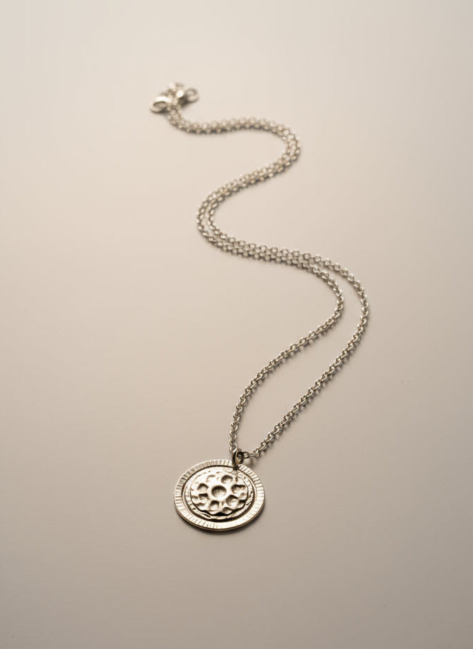 Silver necklace with a round pendant on a textured gray surface