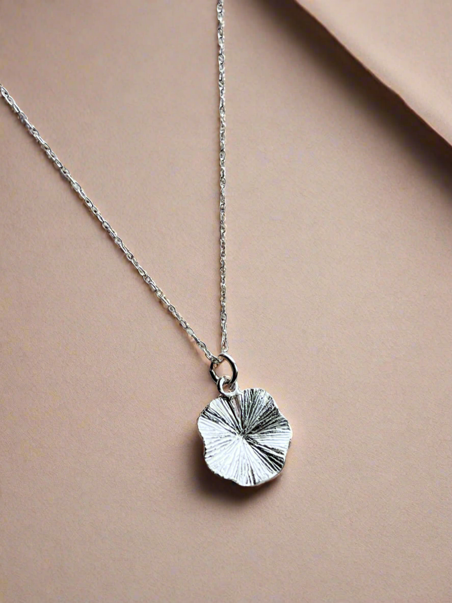 Silver necklace with a leaf-shaped pendant on a beige background