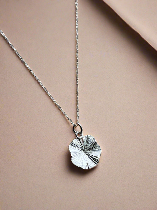 Silver necklace with a leaf-shaped pendant on a beige background