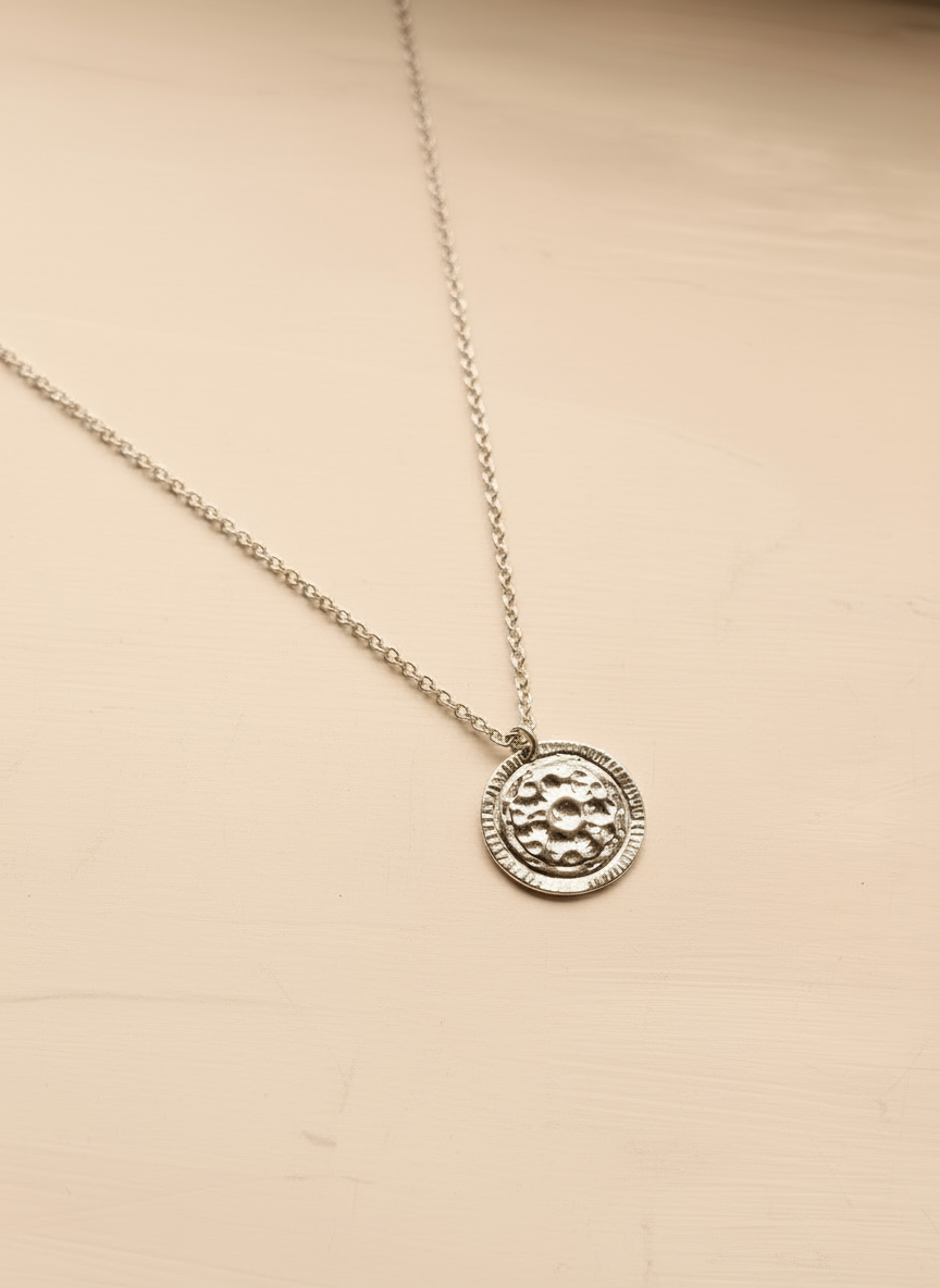 Silver necklace with a round pendant on a beige background