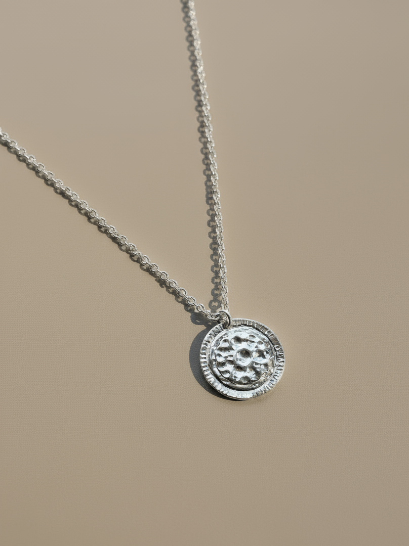 Silver necklace with a round pendant on a beige background
