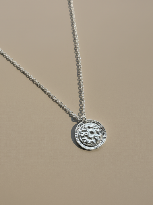 Silver necklace with a round pendant on a beige background