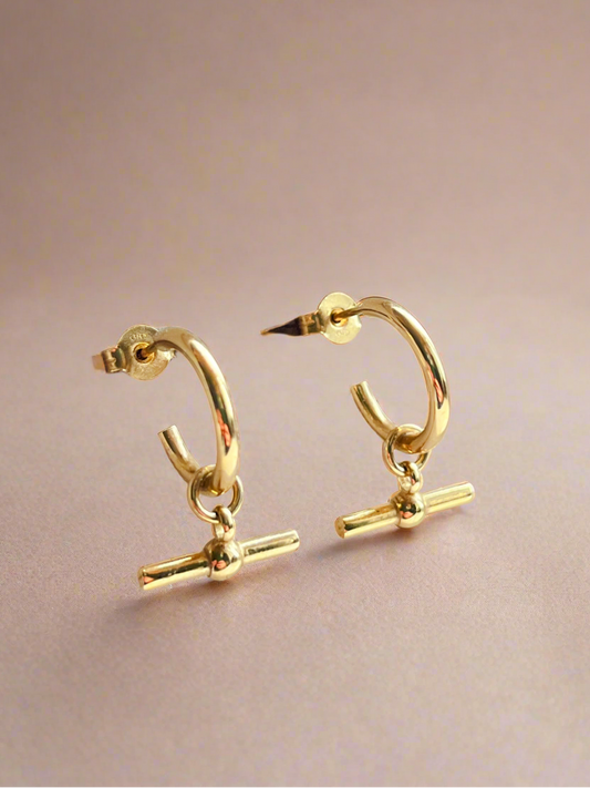 Gold hoop earrings with small vertical bars on a beige background