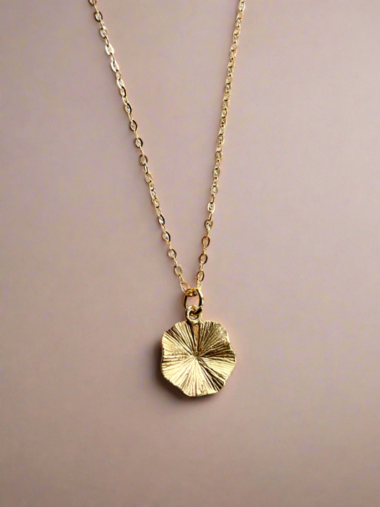 Gold necklace with a circular pendant on a beige background