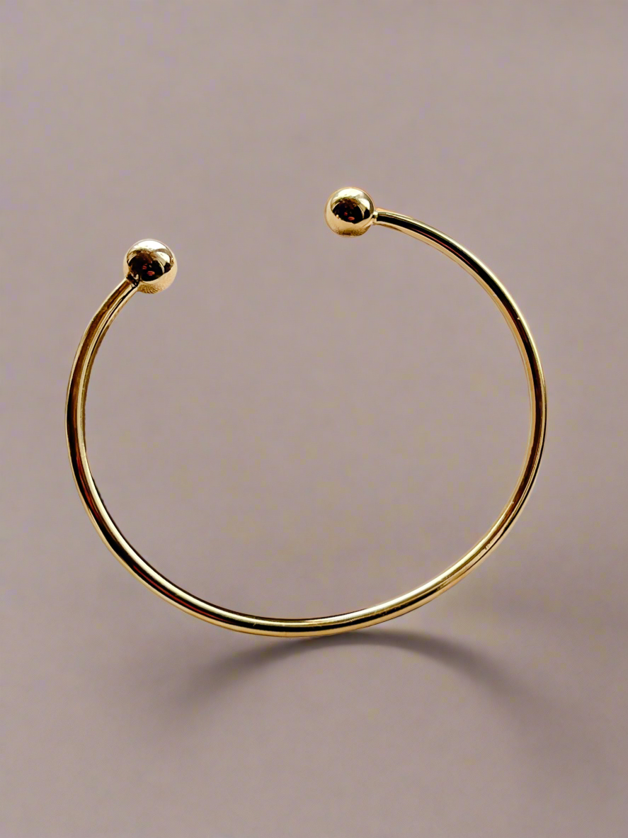 Gold cuff bangle bracelet with on a gray background