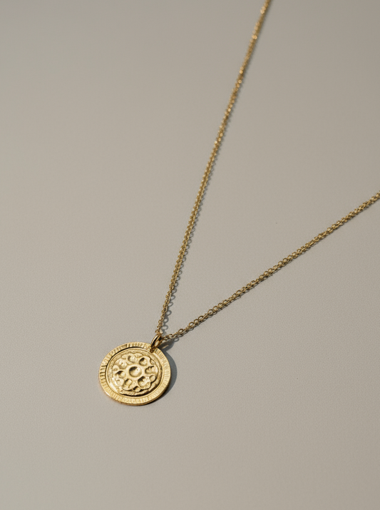 Gold necklace with a round pendant on a gray background