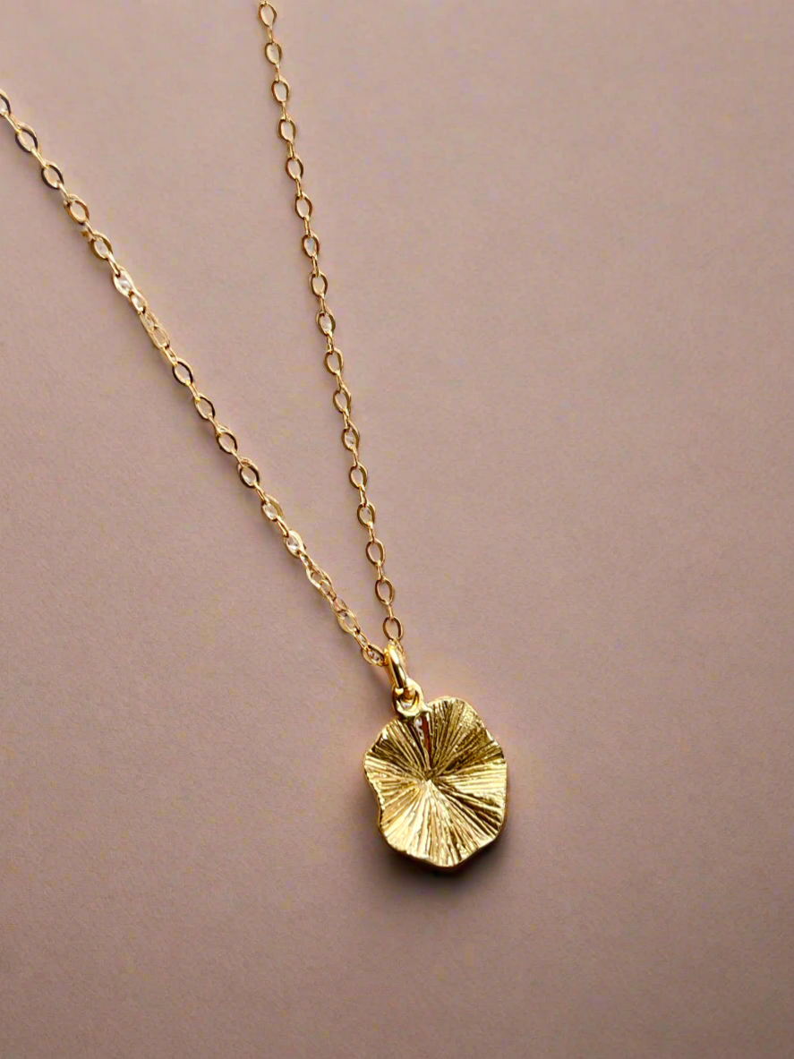 Gold necklace with a leaf-shaped pendant on a beige background