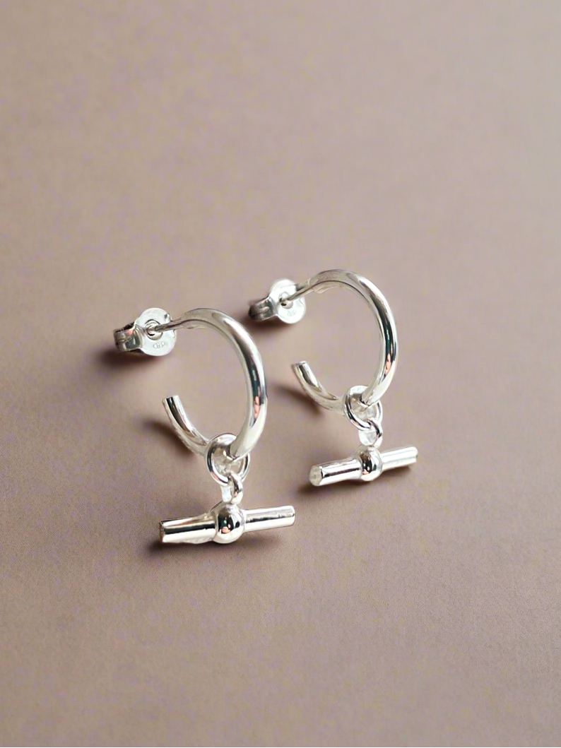 Silver hoop earrings with small charms on a beige background