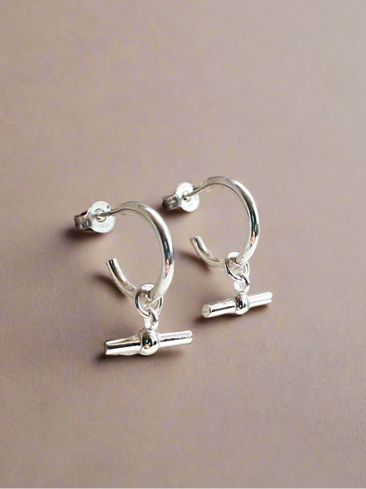 Silver hoop earrings with small charms on a beige background