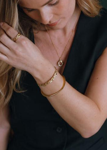 Woman wearing gold jewelry including a necklace, bracelet, and ring.