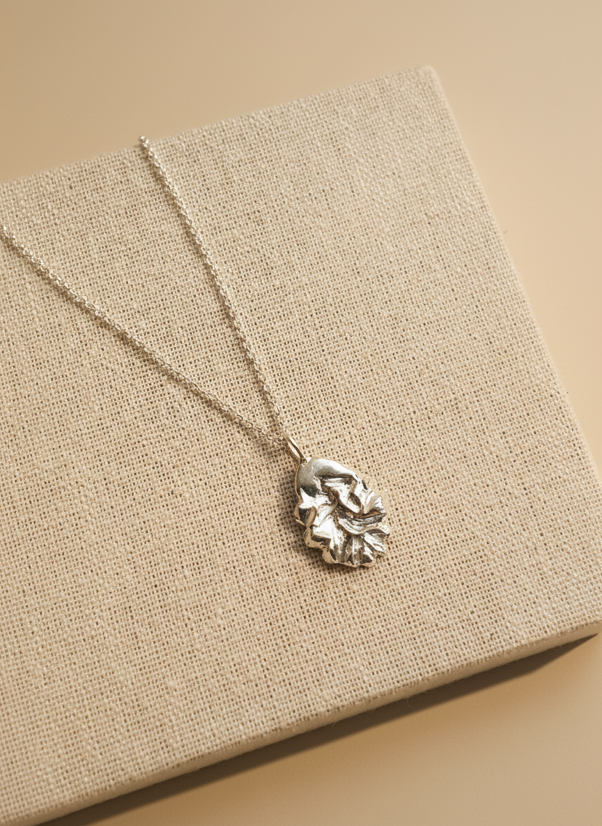 Silver necklace with a leaf pendant on a beige fabric background