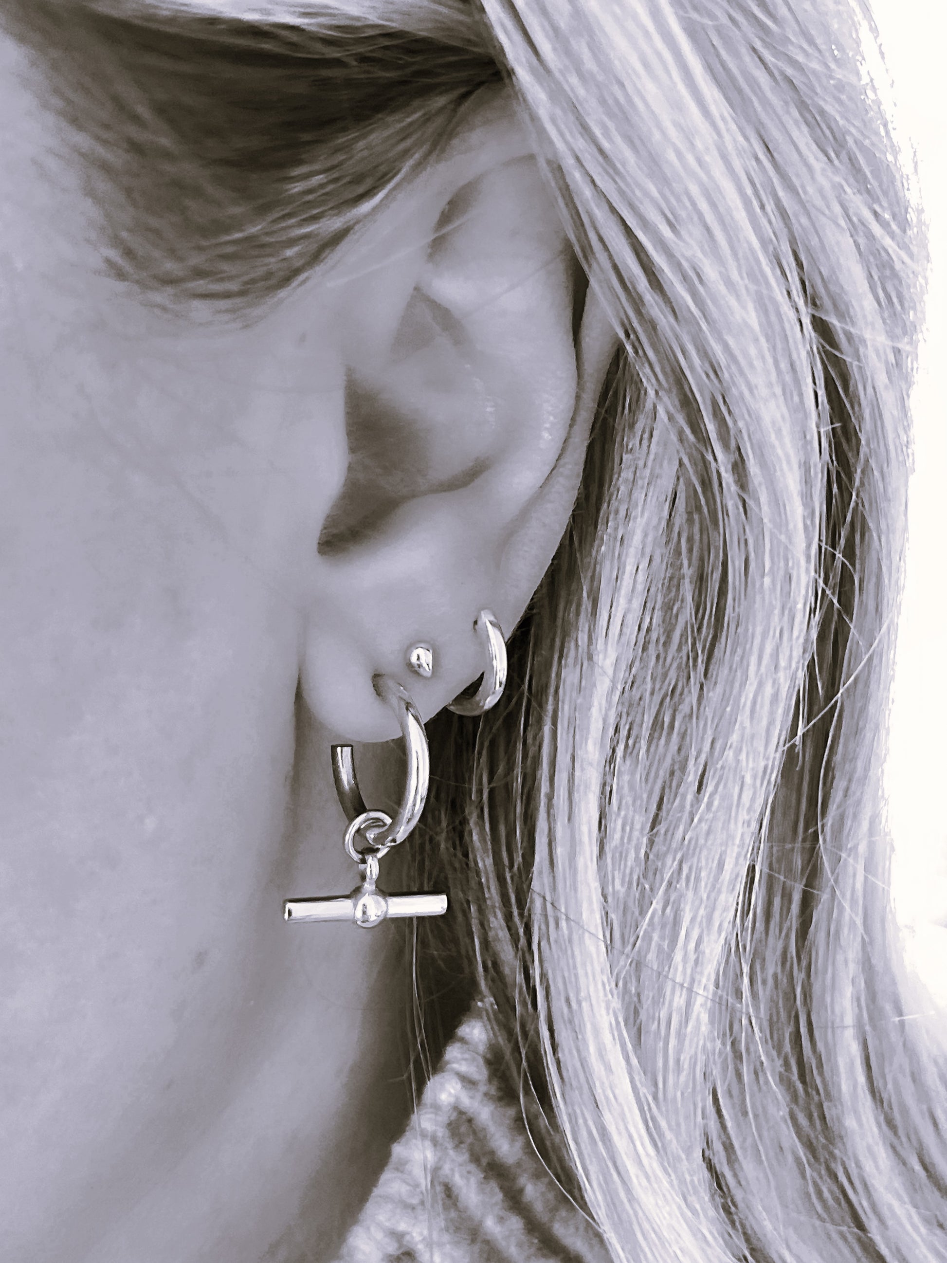 Close-up of a person wearing silver hoop earrings with a small pendant.