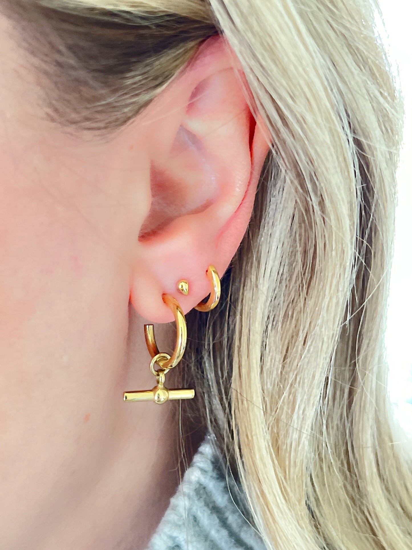 Gold hoop earrings with a T-bar design worn by a person with blonde hair.