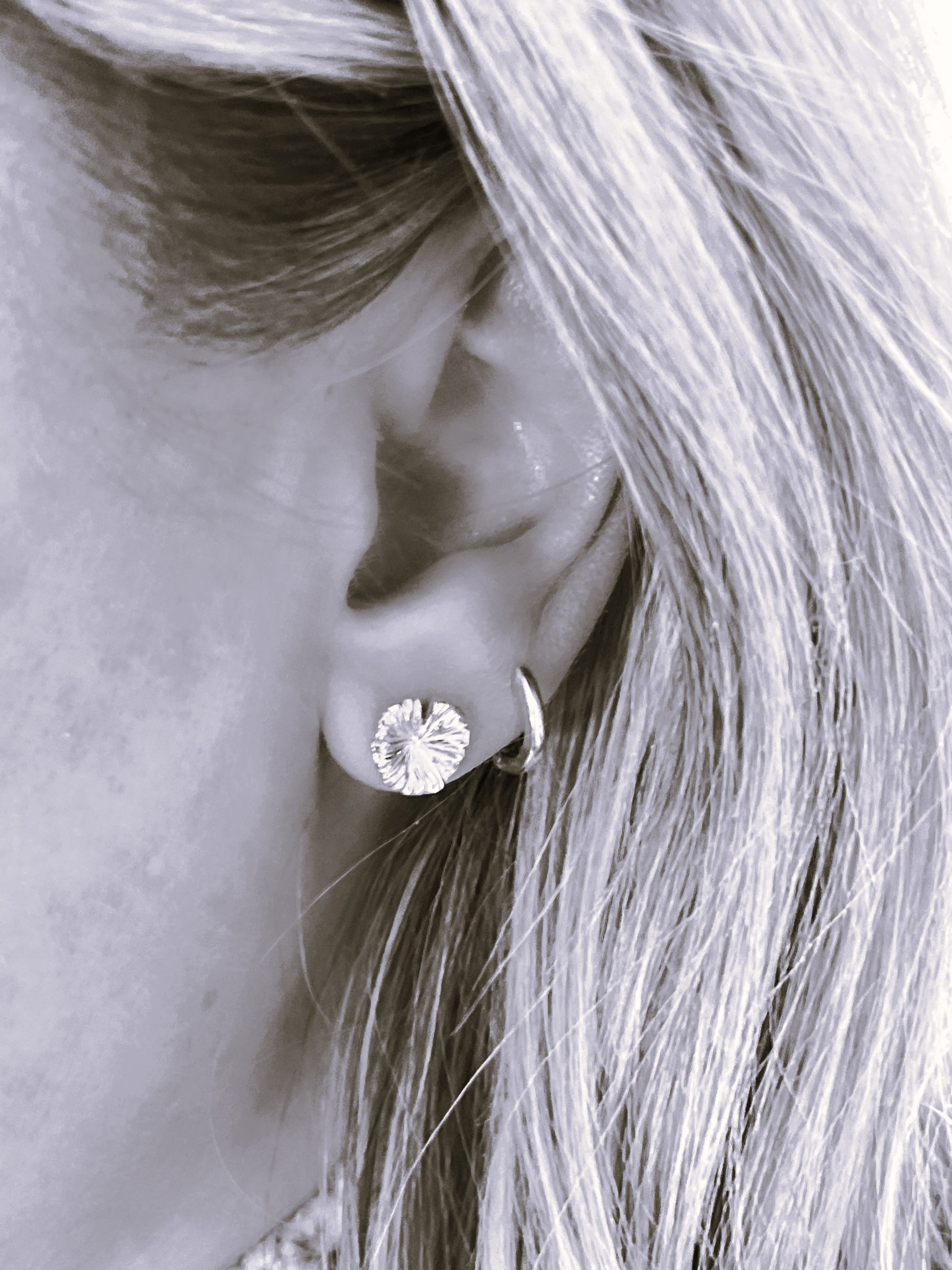 Close-up of a person wearing a silver earring with a diamond-like center.
