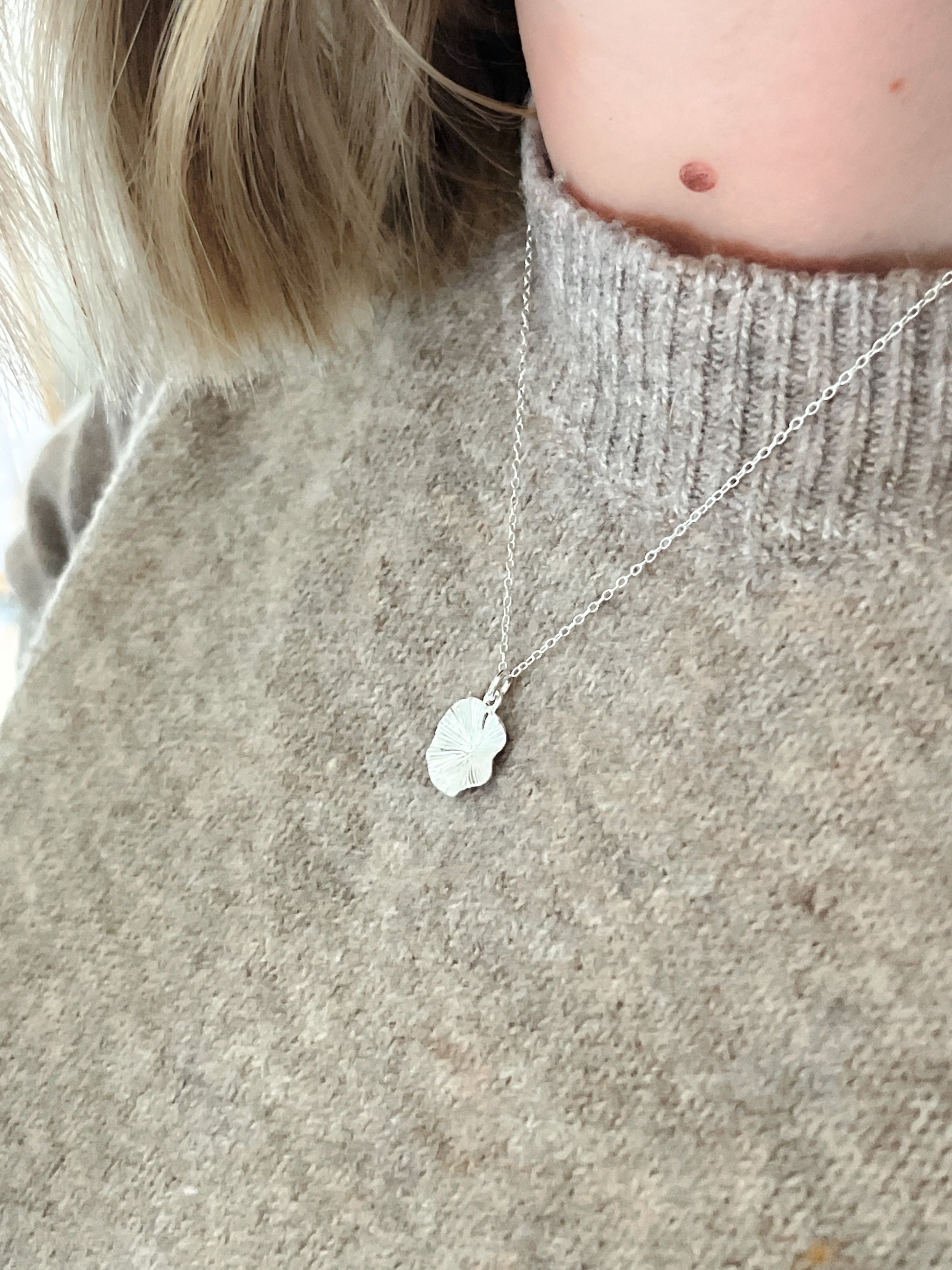 Person wearing a silver necklace with a small pendant on a light gray sweater.
