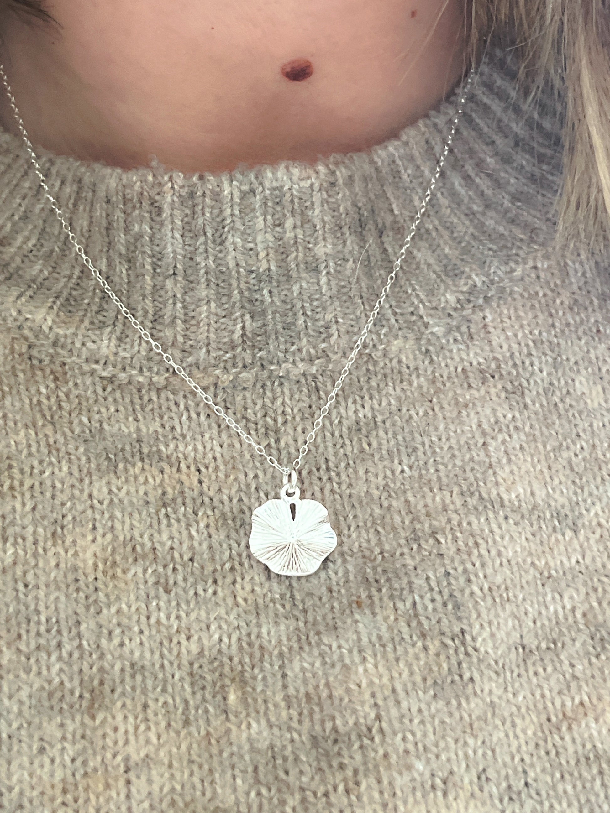 Silver necklace with a sand dollar pendant on a person wearing a gray sweater.