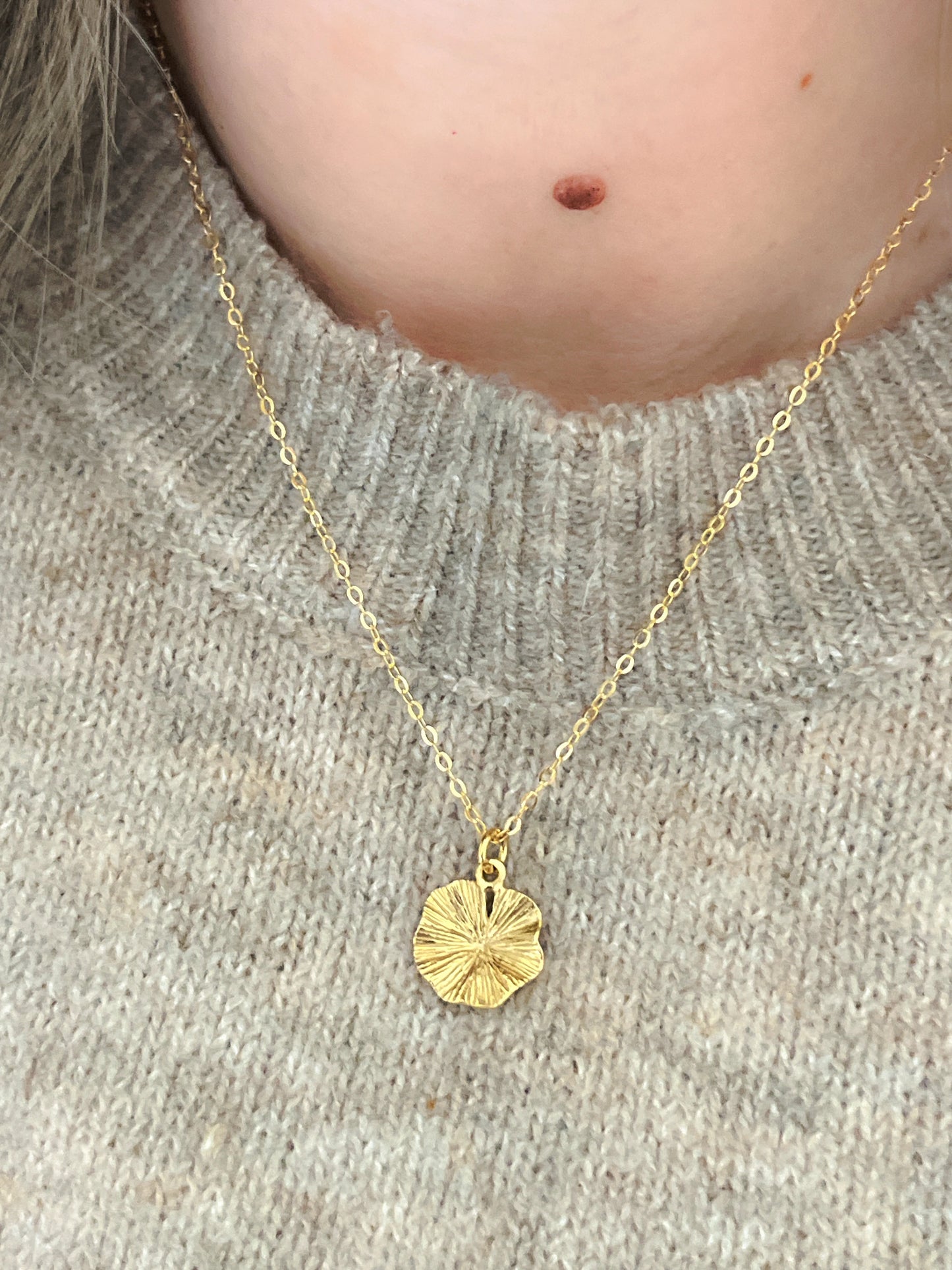 Gold necklace with a round pendant worn by a person on a neutral background