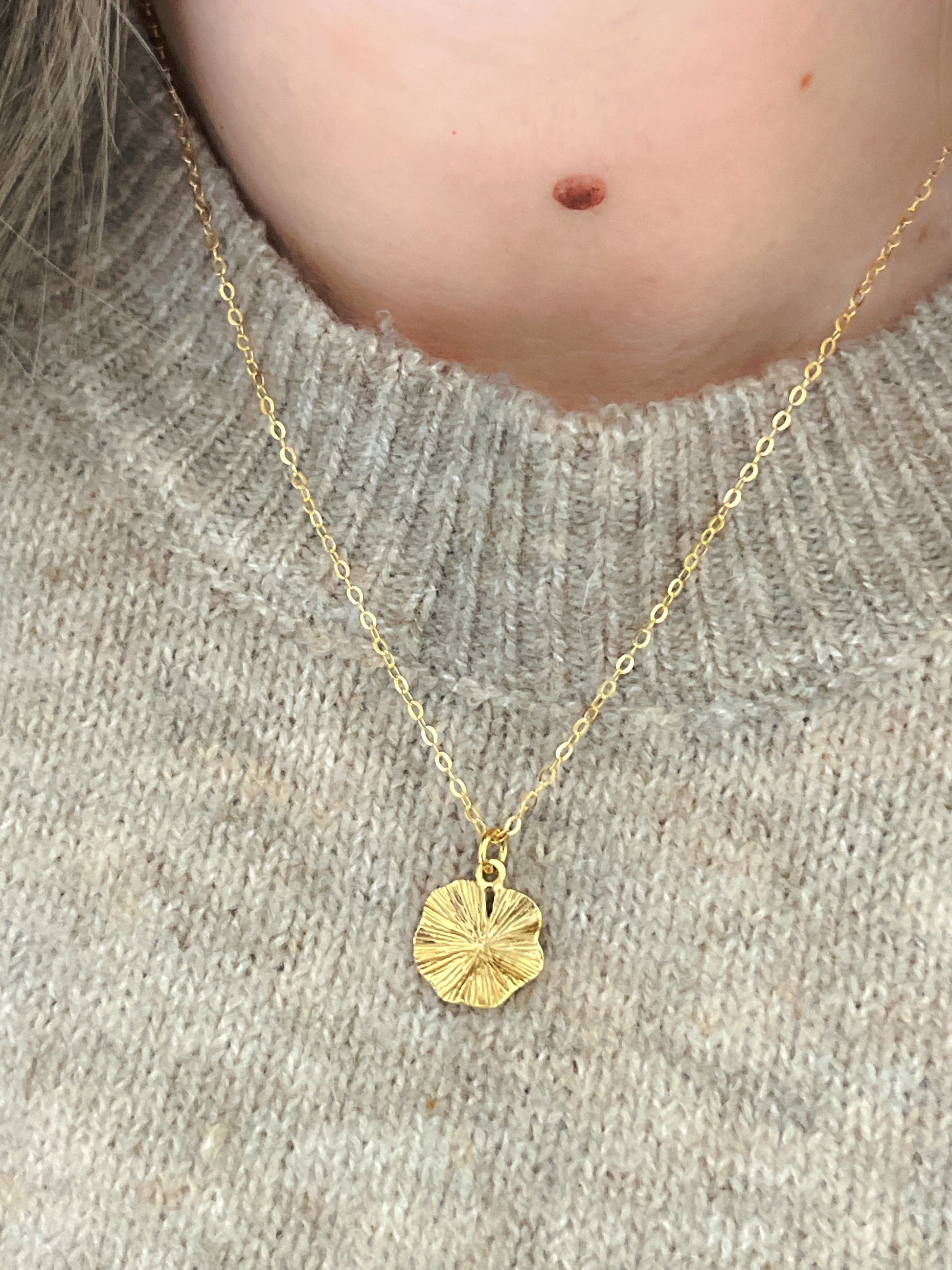 Gold necklace with a round pendant worn by a person on a neutral background