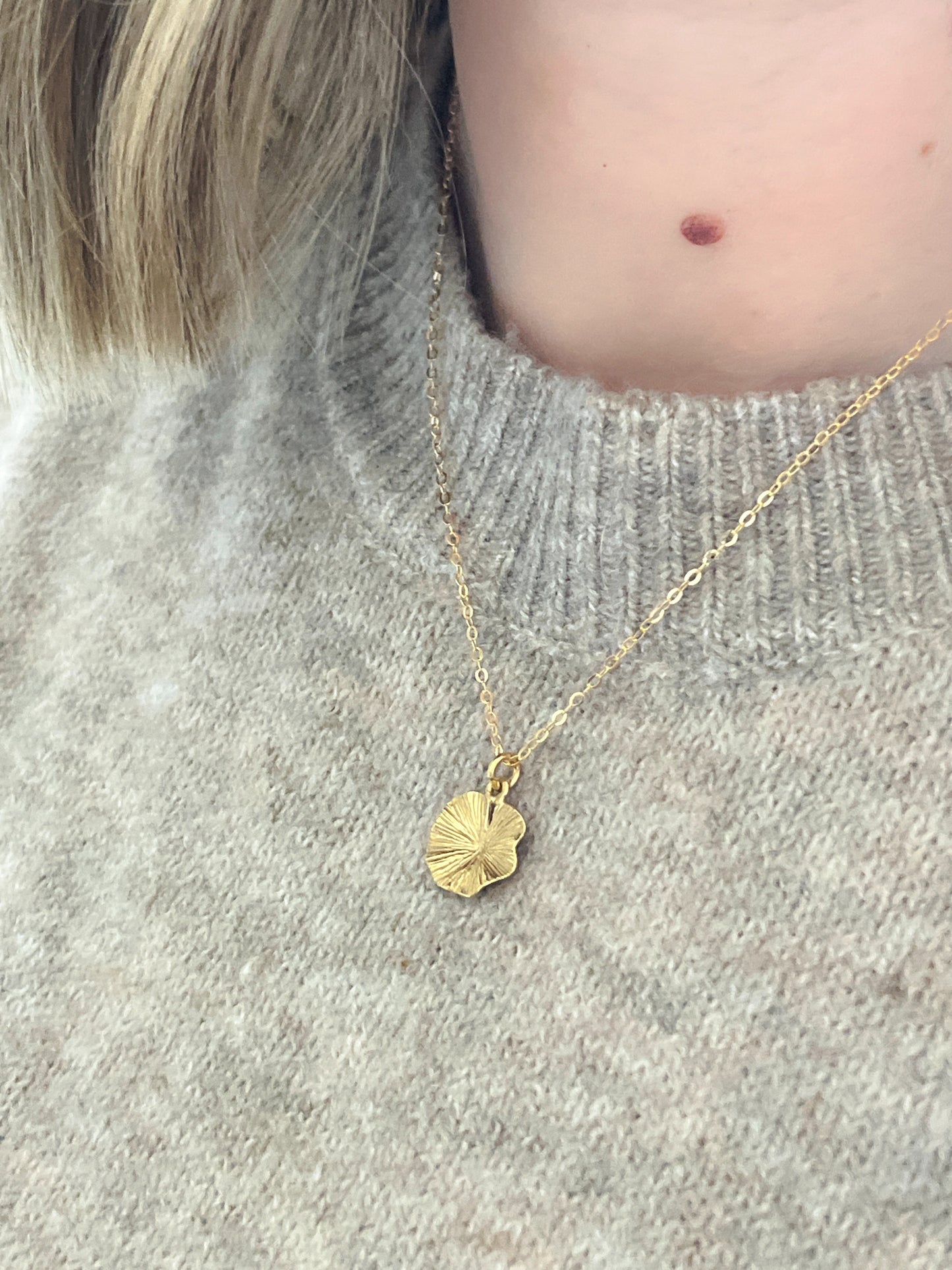 Gold necklace with a pendant worn by a person in a gray sweater.