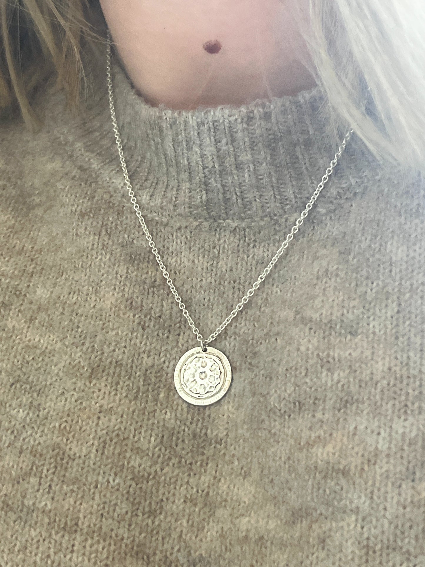 Necklace with a round pendant worn by a person on a gray sweater background