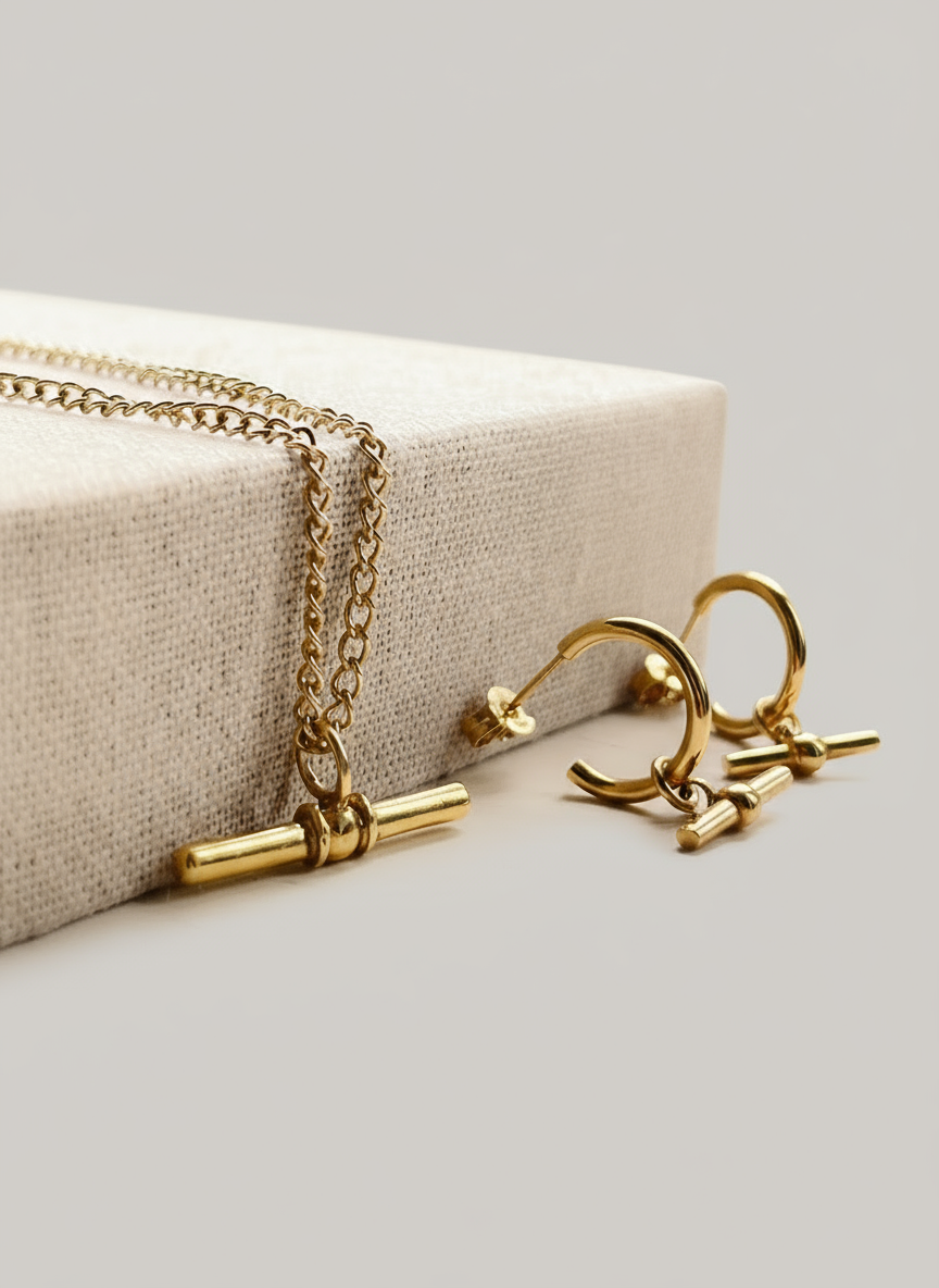 Gold necklace and earrings on a white surface with a neutral background