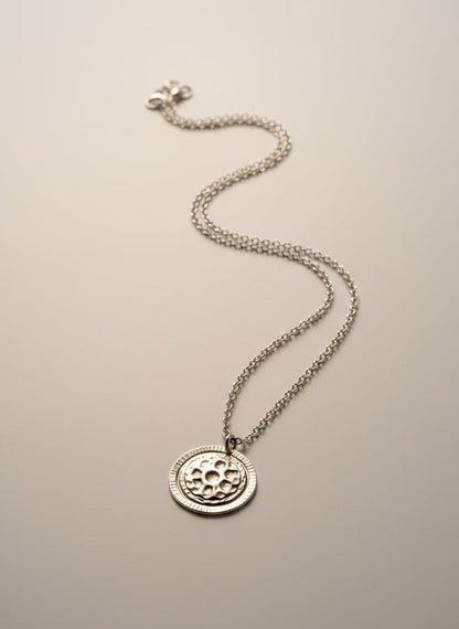 Silver necklace with a round pendant on a textured gray surface