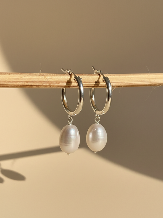 Silver hoop earrings with pearl drops on a white surface