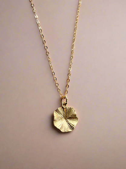 Gold necklace with a circular pendant on a beige background