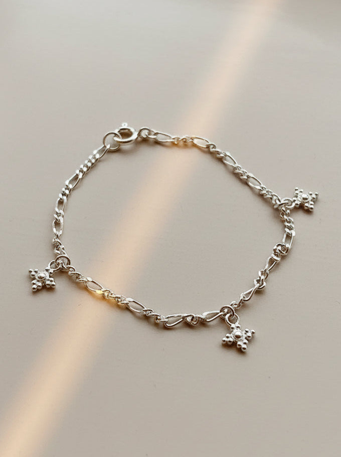Silver bracelet with star charms on a textured beige surface
