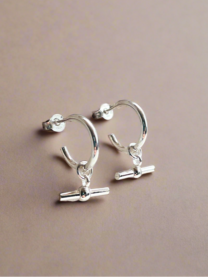 Silver hoop earrings with small charms on a beige background