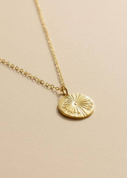 Gold necklace with a circular pendant on a light fabric background