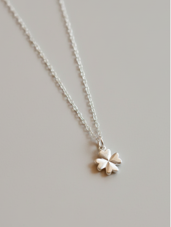 Silver necklace with a four-leaf clover pendant on a light gray background