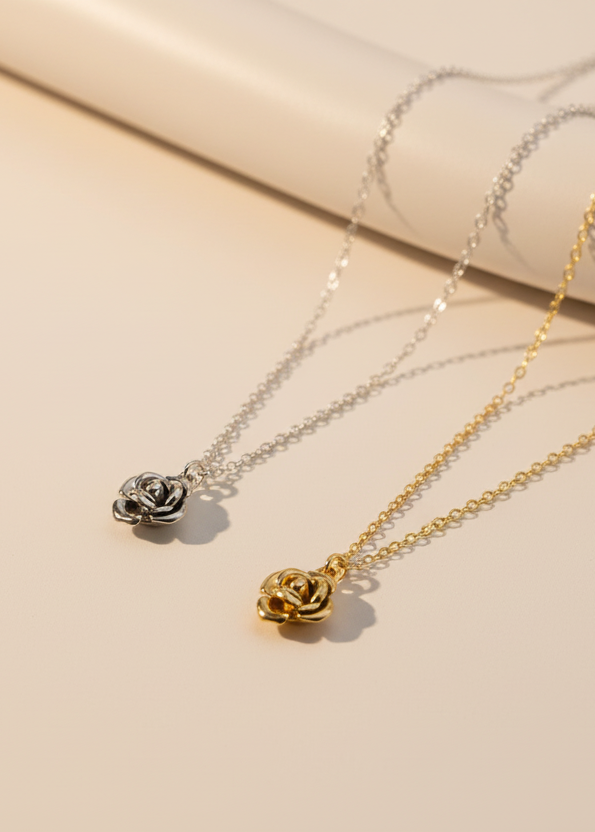 Two rose-shaped pendants on gold and silver chains against a white fabric background
