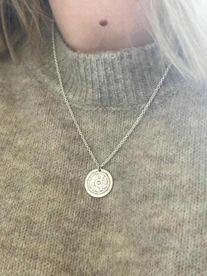 Necklace with a round pendant worn by a person on a gray sweater background